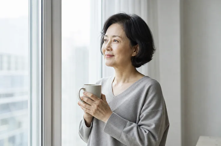 Woman by a bright window holding a warm drink in morning light