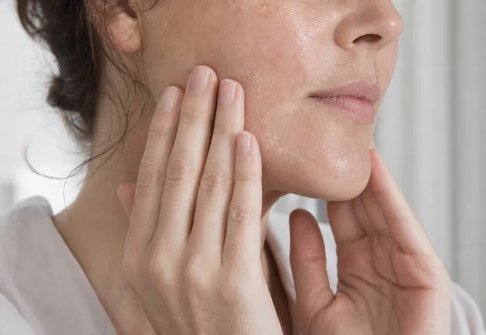 Hands pressing serum into a cheek in natural light